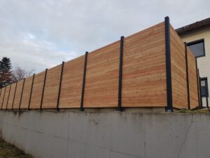 Sichtschutzwand aus Holz mit Pfosten aus Aluminium auf Betonmauer gesetzt.